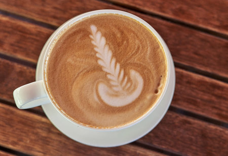 Drawing on brown coffee foam. White saucer and cup with coffee, top view. Background from wooden...