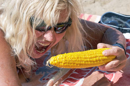The blonde with her mouth wide open wants to bite a large ear of boiled corn with her teeth. Close-upの写真素材