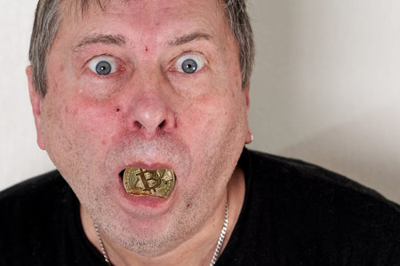 A man holds a coin with the image of bitcoin in his mouth. Goggle eyed freak looking at the camera