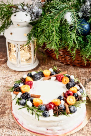 A large round cake decorated with fruits on a Christmas table with a lantern and a spruce branch. Vertical frameの写真素材