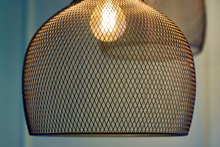 The lamp glows in an openwork metal lampshade in a fine mesh, close up
