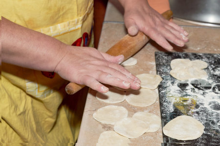 Hands knead the dough on the kitchen table with a wooden rolling pin. Roll out dough for making...