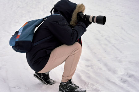 Photographer in winter clothes shoots the camera squatting