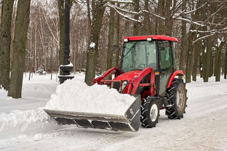 Red tractor with a bucket of praying snow cleans the parkの写真素材