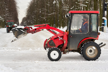 Red tractor with a large bucket removes snow in a city park