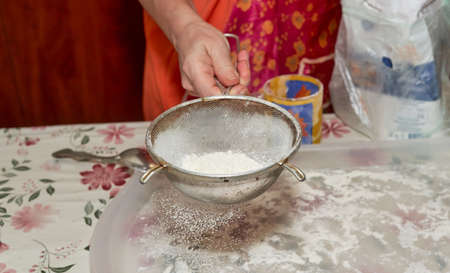 Woman sifts flour through a sieve on a white trayの写真素材