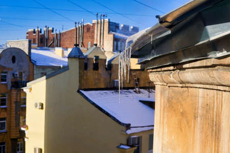 View of snow-covered roofs with spring icicles against blue skyの写真素材