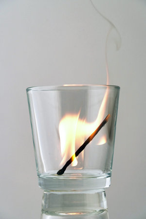 Burning match in a transparent glass on a light background