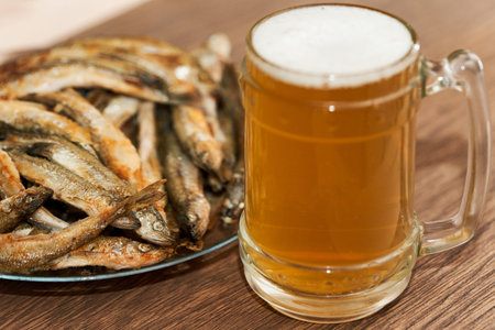 Glass of beer and a plate with small fried fish smelt on the table