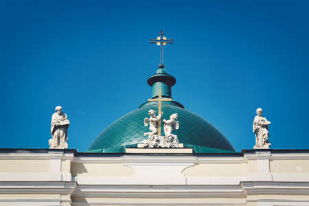 Green dome with a cross and a roof with sculptures against the blue skyの写真素材