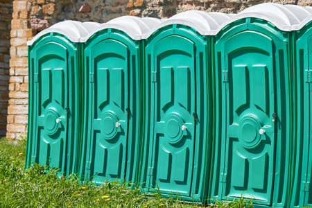 Group of green plastic bio toilet cubicles against a background of stone wall and green grassの写真素材
