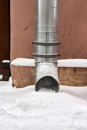 Metal water pipe on the corner of the house is filled with snowの写真素材