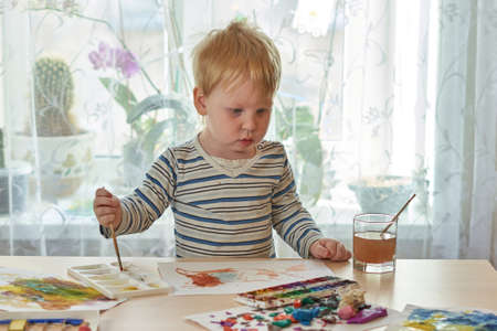 Child draws with paints on a sheet of paperの写真素材