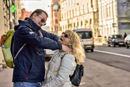 A tall man with a ponytail strangles a woman in the street with his handsの写真素材