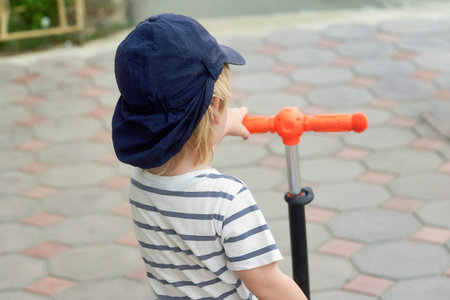 A child in a baseball cap holds the wheel of a scooter, a half-length portrait from the back. Close upの写真素材