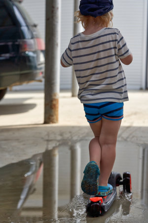 A child on a scooter rides through a puddle. Biking in a puddleの写真素材