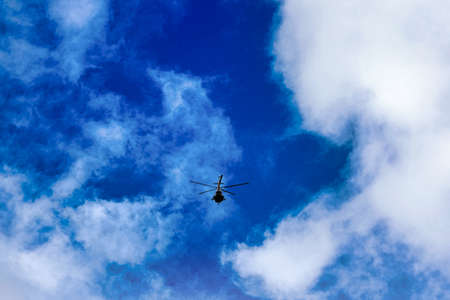 Flying helicopter on the background of clouds and blue sky. Small aircraftの写真素材