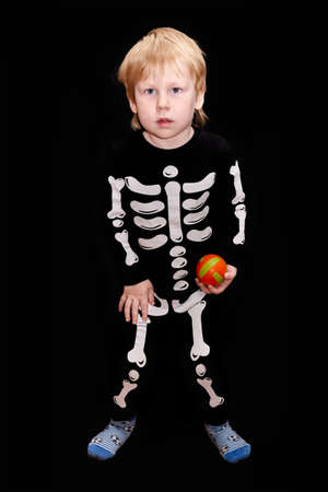 child of four years old in a skeleton costume with an orange ball in his hand on black background. Children fears and scaresの写真素材