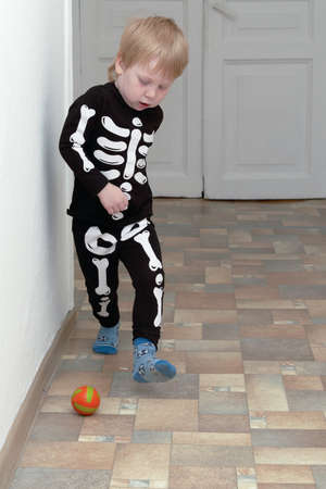 A child in a skeleton costume plays football in the hallway of the house. Children outdoor gamesの写真素材