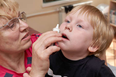 Grandma drips nose drops to child, treating children at homeの写真素材