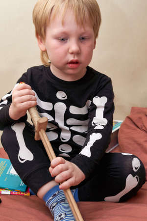 A child in a skeleton costume with a wooden sword sits on the couchの写真素材
