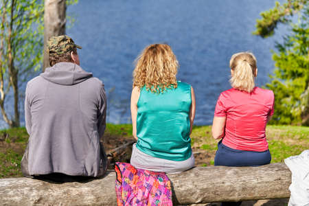 A man and two women sit on the shore of a forest lakeの写真素材