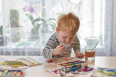 A child with a paintbrush bent over a box of paintsの写真素材