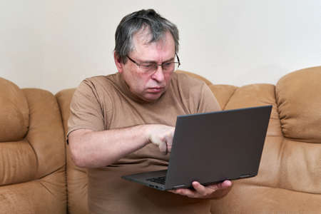 A man at the age of sitting on Devani looks through the news on a laptop.の写真素材