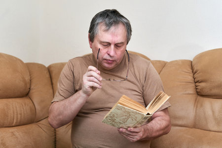 A man of age sitting on the Devani is reading a bookの写真素材