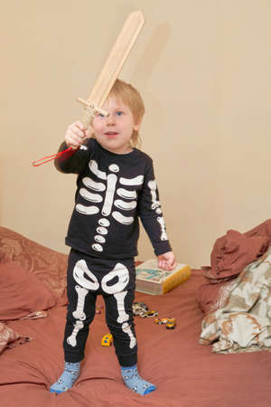A child in a skeleton costume with a wooden sword plays on the couchの写真素材