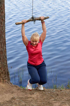 Middle aged woman in sportswear hanging on a stick with a rope above the waterの写真素材