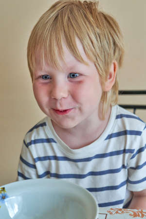Smiling child sits in front of an empty clean plate. Child waiting for foodの写真素材
