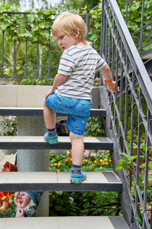 A little boy climbs up the stairs to the house from the garden. The child climbs the stairs.の写真素材