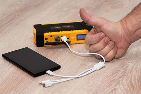 Hand with a raised thumb next to a smartphone charging from a plunging powerbankの写真素材