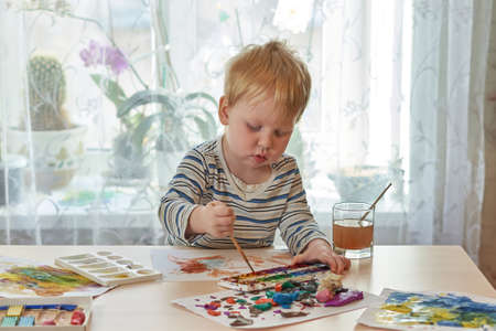 Child draws with paints on a sheet of paperの写真素材