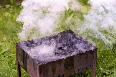 Firing up an old rusty metal barbecue grill, smoke and fire. Preparing for an outdoor barbecueの写真素材