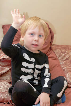 A child in a skeleton costume sits on the couch waving his hand in greetingの写真素材