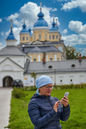 A believing parishioner with a telephone against the background of the Orthodox Church. Woman with smartphone at the templeの写真素材