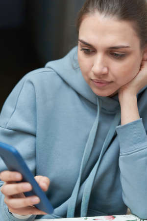 A beautiful brunette with long hair combed back looks into her smartphoneの写真素材