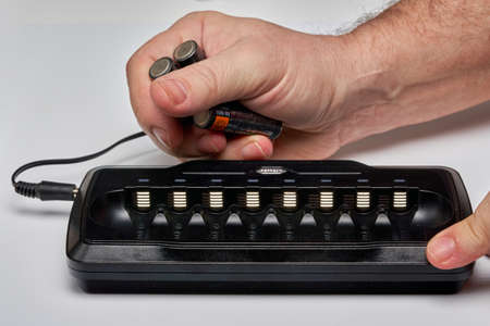 Hands insert AA batteries into black long chargerの写真素材