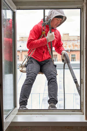 A window washer in climbing gear hangs in the window openingの写真素材