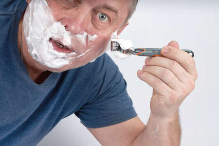A mans face in shaving foam shaves with a safety razorの写真素材