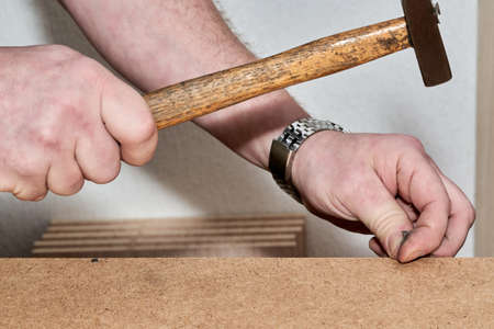 Hand with hammer hammer hammers nail when assembling furnitureの写真素材