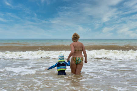 A woman and a child walk into the sea holding hands, view from the backの写真素材