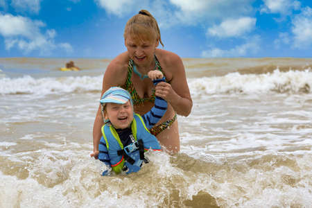 A woman takes a child in a life jacket out of the stormy seaの写真素材