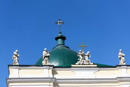 Green dome with a cross and a roof with sculptures against the blue skyの写真素材