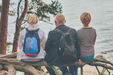 A man and two women sit on the shore of a forest lakeの写真素材