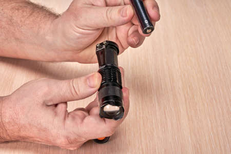 Hands hold a small black flashlight and replace the battery in itの写真素材