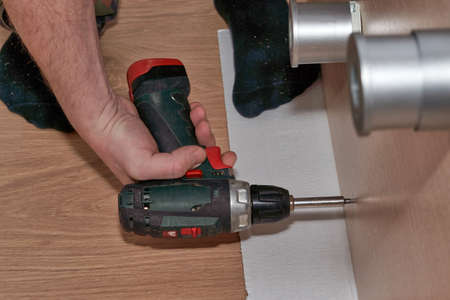 A hand with a screwdriver twists the screw into a wooden slabの写真素材