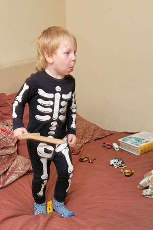A child in a skeleton costume with a wooden sword plays on the couchの写真素材